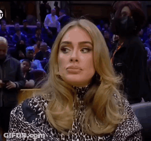 A Woman Wearing A Leopard Print Top Is Sitting In Front Of A Crowd GIF