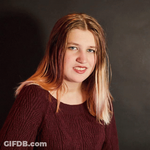 A Woman Wearing A Maroon Sweater Is Smiling And Looking At The Camera GIF