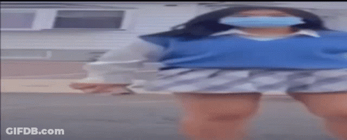 A Woman Wearing A Mask And A Blue Sweater Is Dancing In Front Of A House . GIF