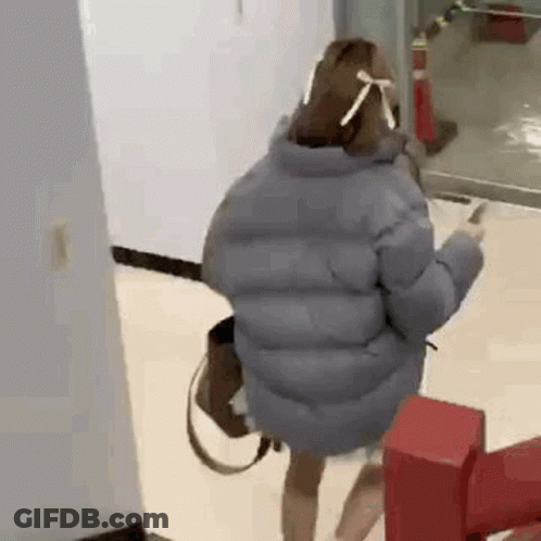 A Woman Wearing A Mask And A Jacket Is Standing In A Hallway . GIF