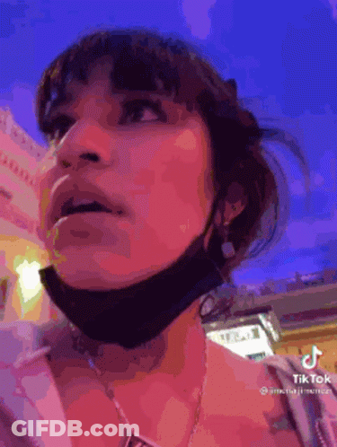 A Woman Wearing A Mask And A Necklace Is Looking Up At Something . GIF