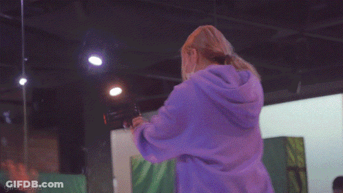 A Woman Wearing A Mask And A Purple Hoodie Is Standing In A Room GIF