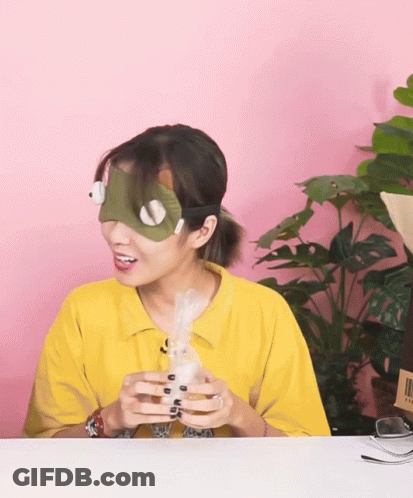 A Woman Wearing A Mask And A Yellow Shirt Is Holding A White Object GIF