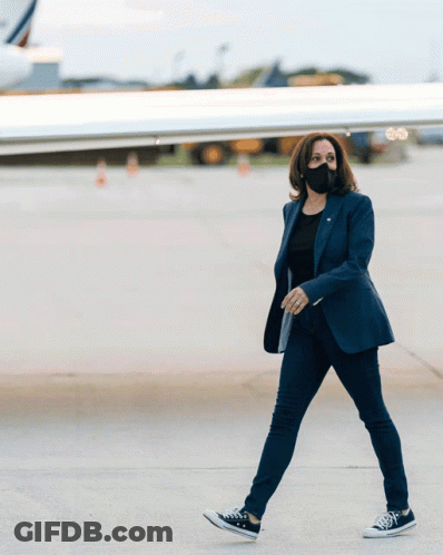 A Woman Wearing A Mask And Converse Shoes Walks On An Airport Tarmac GIF