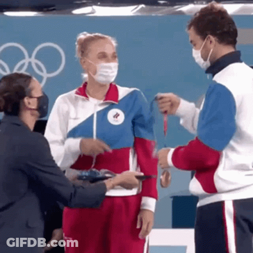 A Woman Wearing A Mask Is Being Handed A Medal By Two Men GIF