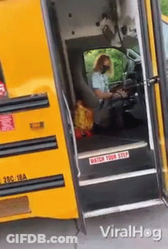 A Woman Wearing A Mask Is Driving A School Bus With The Door Open . GIF