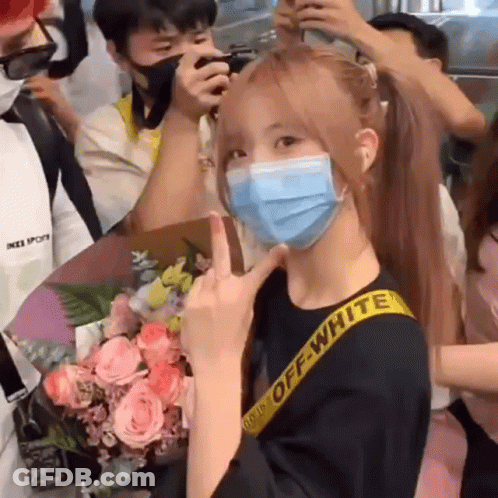 A Woman Wearing A Mask Is Giving The Middle Finger In Front Of A Crowd . GIF