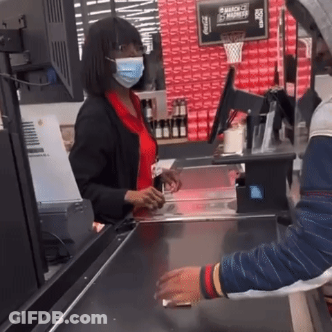 A Woman Wearing A Mask Is Standing At A Cash Register In Front Of A Sign That Says Coca Cola GIF