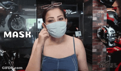 A Woman Wearing A Mask Is Standing In Front Of A Sign That Says Mask GIF