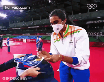A Woman Wearing A Mask Is Standing On A Red Carpet And Signing A Hat . GIF