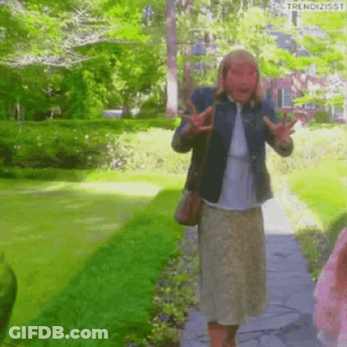 A Woman Wearing A Mask Is Walking Down A Path In The Park . GIF