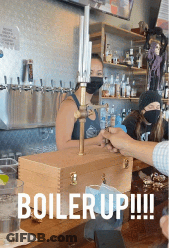 A Woman Wearing A Mask Stands Behind A Wooden Box That Says " Boiler Up " GIF