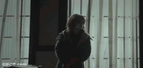 A Woman Wearing A Mask Stands In Front Of A Window In A Dark Room . GIF