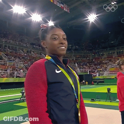 A Woman Wearing A Medal Around Her Neck Stands In Front Of A Crowd At The Olympics GIF