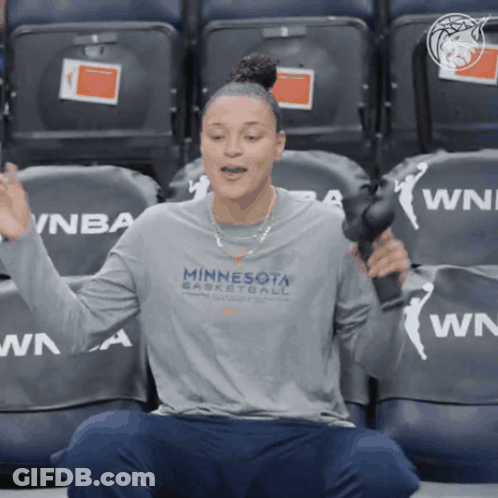 A Woman Wearing A Minnesota Basketball Shirt Is Sitting In A Stadium GIF