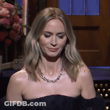 A Woman Wearing A Necklace And A Black Dress Is Smiling GIF