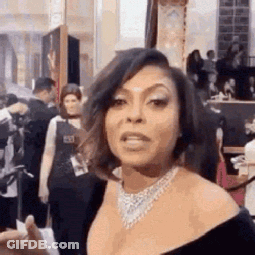 A Woman Wearing A Necklace And A Black Dress Is Standing In Front Of A Crowd . GIF