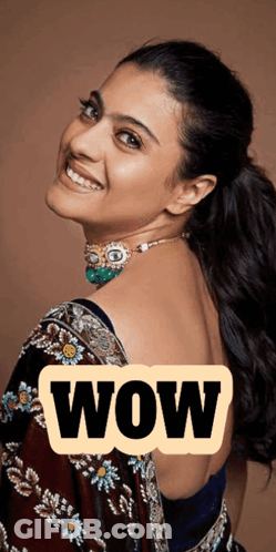 A Woman Wearing A Necklace And A Blue Blouse Is Smiling With The Word Wow Behind Her GIF
