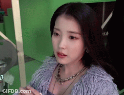 A Woman Wearing A Necklace And A Purple Sweater Looks At The Camera GIF