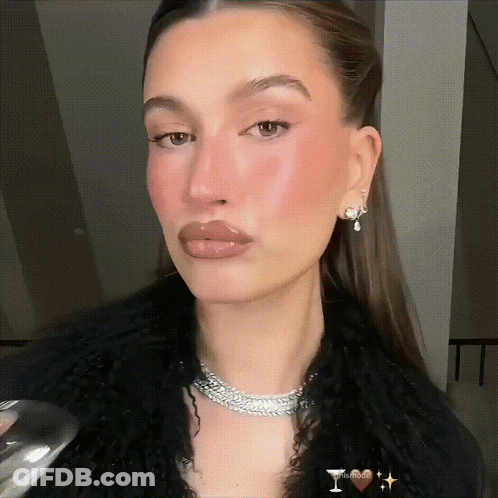 A Woman Wearing A Necklace And Earrings Holds A Glass Of Wine In Her Hand GIF