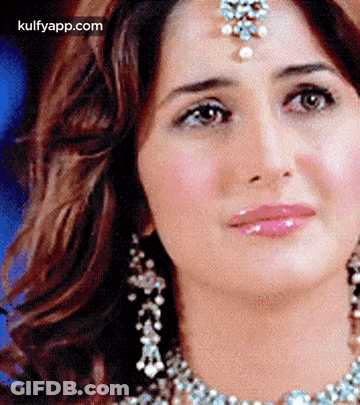 A Woman Wearing A Necklace And Earrings Is Looking At The Camera . GIF