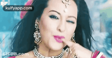 A Woman Wearing A Necklace And Earrings Is Making A Funny Face With Her Finger On Her Lips . GIF