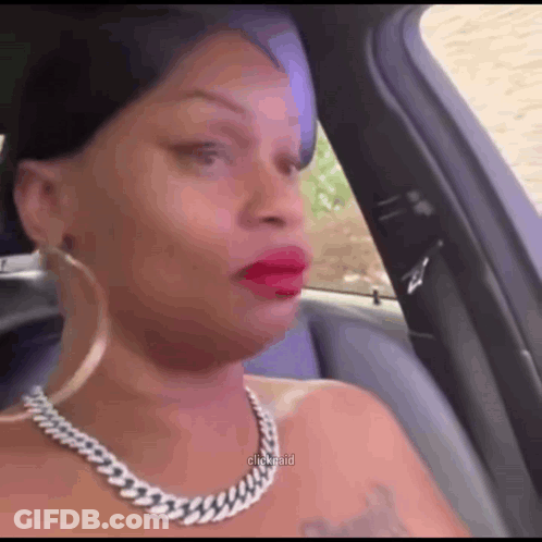 A Woman Wearing A Necklace And Earrings Is Sitting In A Car Making A Funny Face . GIF