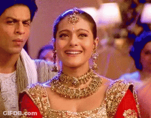 A Woman Wearing A Necklace And Earrings Is Smiling While Standing Next To A Man . GIF