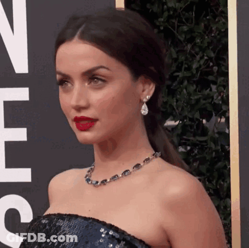 A Woman Wearing A Necklace And Earrings Is Standing In Front Of A Sign That Says ' N ' On It GIF