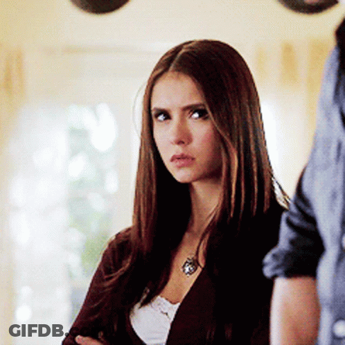 A Woman Wearing A Necklace Is Standing Next To A Man With Her Arms Crossed GIF