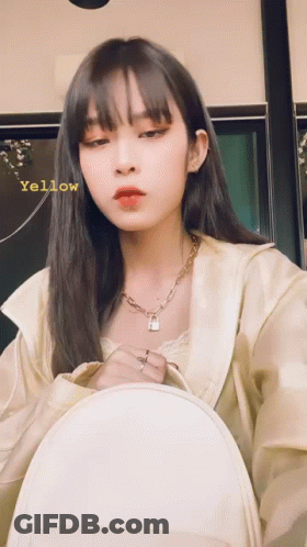 A Woman Wearing A Necklace With A Padlock On It Is Holding A White Backpack And Has The Word Yellow Written On Her Face GIF