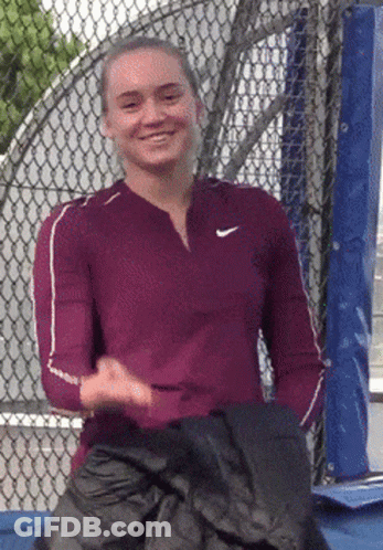 A Woman Wearing A Nike Shirt Is Smiling And Holding A Black Jacket GIF