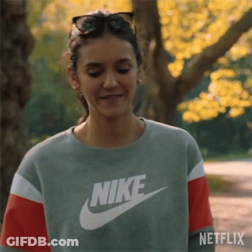 A Woman Wearing A Nike Sweatshirt And Sunglasses Is Smiling In A Park . GIF