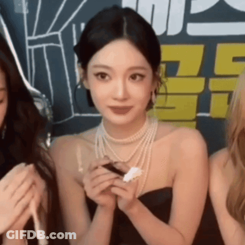A Woman Wearing A Pearl Necklace And A Black Dress Is Holding A Piece Of Paper . GIF