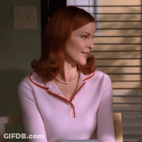 A Woman Wearing A Pearl Necklace And A Pink Shirt GIF