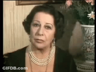A Woman Wearing A Pearl Necklace And Earrings Is Looking At The Camera . GIF