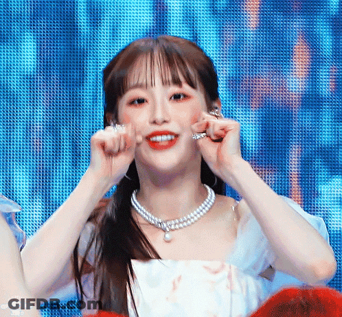 A Woman Wearing A Pearl Necklace And Earrings Looks At The Camera GIF