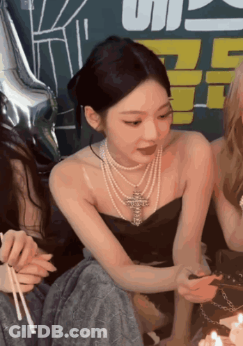A Woman Wearing A Pearl Necklace Is Sitting Next To A Cake With Candles GIF