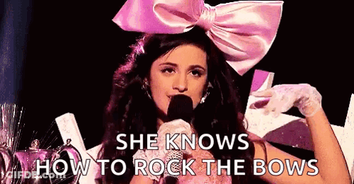 A Woman Wearing A Pink Bow Is Holding A Microphone And Talking Into It . GIF