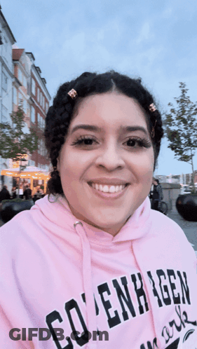 A Woman Wearing A Pink Copenhagen Hoodie Smiles GIF