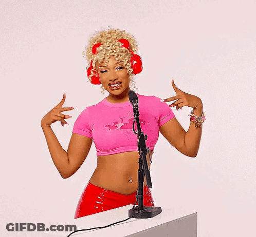 A Woman Wearing A Pink Crop Top And Red Headphones Is Standing In Front Of A Microphone GIF