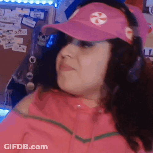 A Woman Wearing A Pink Hat And Headphones Is Making A Funny Face . GIF