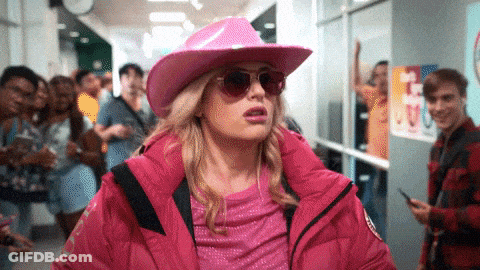 A Woman Wearing A Pink Hat And Sunglasses Is Walking Down A Hallway . GIF