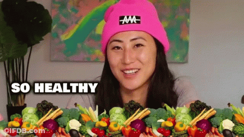 A Woman Wearing A Pink Hat Is Surrounded By Vegetables And The Words So Healthy Are Above Her . GIF
