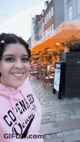 A Woman Wearing A Pink Hoodie That Says Copenhagen Denmark Is Smiling GIF