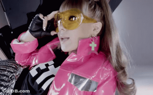 A Woman Wearing A Pink Jacket And Yellow Sunglasses Has A Cross On Her Earring GIF