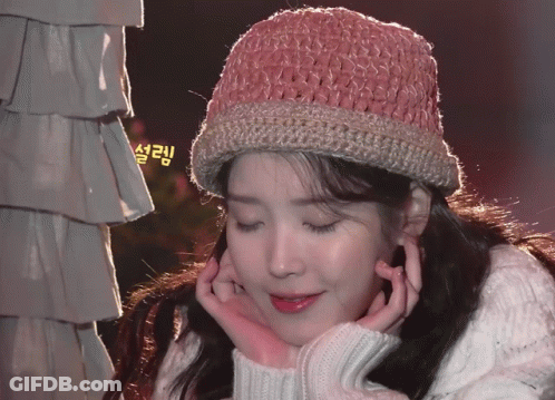 A Woman Wearing A Pink Knitted Hat And A White Sweater Has Her Hands On Her Face GIF