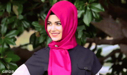 A Woman Wearing A Pink Scarf And A Black Shirt Smiles For The Camera GIF
