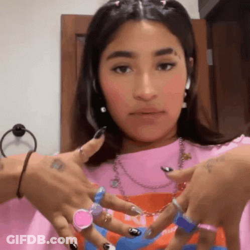 A Woman Wearing A Pink Shirt And A Bunch Of Rings On Her Hands . GIF