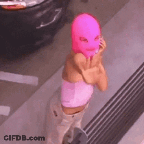 A Woman Wearing A Pink Ski Mask Is Standing In Front Of A Car . GIF